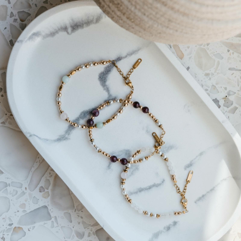 Bransoletka z granatu, z pereł, awenturynu i kwarcu różowegow zestawie z innymi bransoletkami z kamieni naturalnych na marmurowym talerzu – kolekcja premium